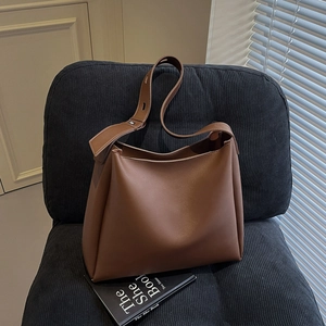 Detail shot of brown vintage PU leather tote bag with adjustable strap on a textured seat