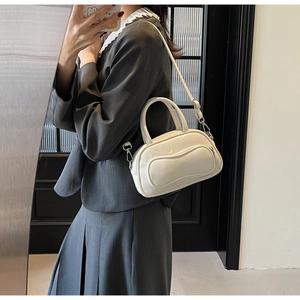 Détail du sac Boston en cuir verni blanc porté avec une robe tailleur grise élégante