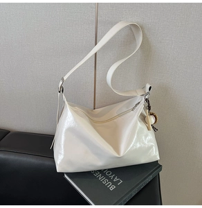 Detail of cream hobo bag on sofa showing glossy wrinkled leather and baseball charm