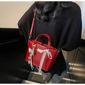 Detailed back view of a red patent leather bucket bag with silver bow charm and lace