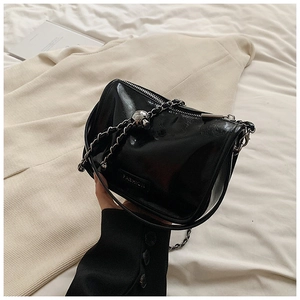 Detail of glossy black handbag with silver chain strap and skull charm detail