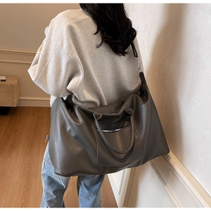 Sac de voyage en similicuir gris foncé porté à l'épaule dans un intérieur chaleureux