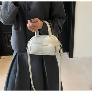Sac bandoulière Boston blanc cassé avec poche vague porté sur un blazer gris chic