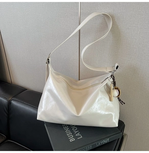 Detail of a creamy white glossy tote bag with a baseball charm on a leather sofa