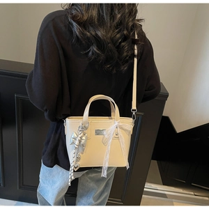 Detail of beige PU leather bucket bag with silver bow charm and lace ribbon handle