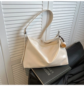 Detail view of cream white PU leather tote bag with round charm and adjustable strap