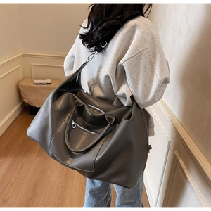 Femme portant un grand sac de voyage gris foncé avec bandoulière en intérieur moderne