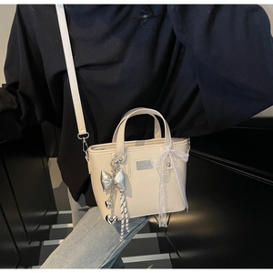 Detail of cream leather bucket bag with silver bow charm and lace bow accessory