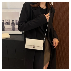 Detail of a creamy white rectangular crossbody bag with silver chain and metal lock closure