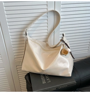 Detail of cream white leather tote bag with creative baseball charm and adjustable strap