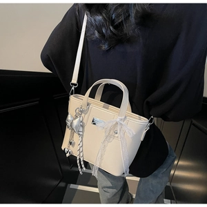 Close-up of cream bucket bag with lace bow, heart pendant, and textured leather finish