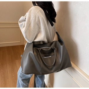 Détail d'un grand sac de voyage gris avec bandoulière porté par un mannequin