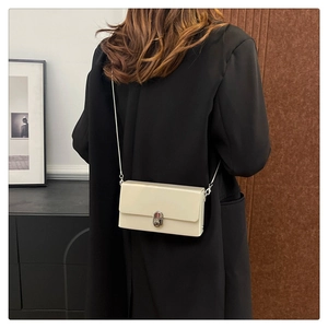 Detail of a beige patent leather crossbody bag with silver twist lock and chain strap