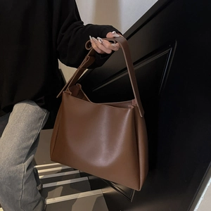 Close-up of brown matte leather tote bag with wide shoulder strap on a minimalist model
