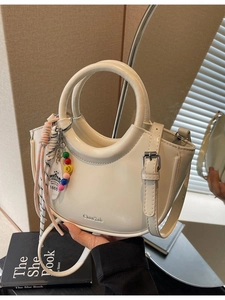 Fashionable cream-colored semi-circular handbag with beaded charm and silk scarf detail