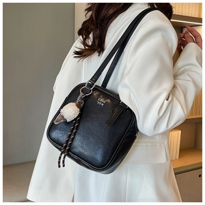 Detail of a black square underarm bag with a white plush ice cream charm on a white blazer