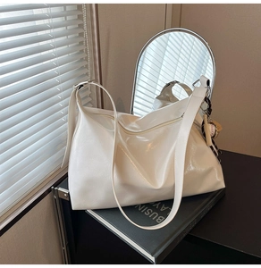 Detail of white glossy PU leather tote bag with baseball charm on a structured shoulder bag