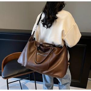 Détail du sac de voyage en cuir marron foncé avec texture lisse et poche zippée argent