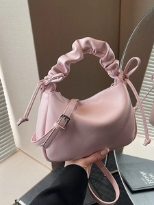 Pink PU leather dumpling bag with ruched handle and side bow ties on a mirror