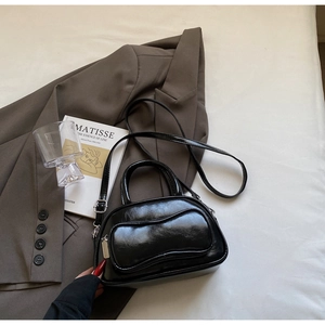 Détail du sac Boston noir brillant avec ferrures argentées sur un fond de lit élégant