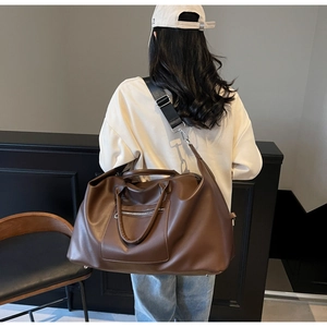 Grand sac de voyage en cuir marron foncé avec bandoulière porté par un mannequin