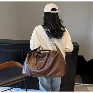 Détail d'un grand sac de voyage marron avec poche zippée argentée et large bandoulière nylon