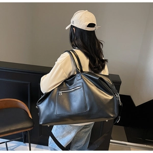 Vue détaillée d'un grand sac de voyage noir en similicuir brillant porté par un mannequin