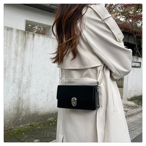 Detail of a black crossbody box bag featuring silver metallic lock and chain strap on model