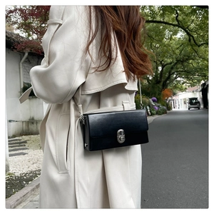 Detail of a black leather crossbody box bag with silver twist lock and chain strap