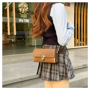 Detail of a brown leather crossbody box bag with silver metal buckle on a model