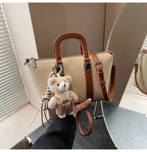 Detail of a beige woven bucket bag with brown leather handles and a cute teddy bear charm