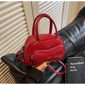 Détail du sac Boston en cuir verni rouge avec fermeture éclair ondulée sur sofa