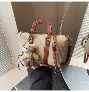Detail of woven beige bucket bag featuring brown leather straps and a cute teddy bear charm