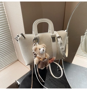 Detail of cream woven bucket bag with leather strap and cute bear plush pendant