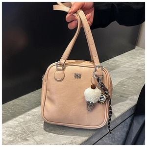Detail of light beige square handbag with leather texture, logo and decorative charms