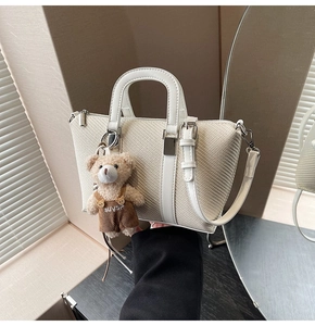 Detail of cream woven bucket bag featuring a cute teddy bear charm and silver hardware