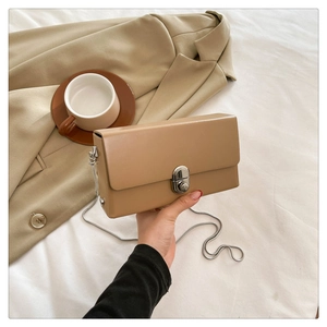 Handheld khaki chain crossbody bag with silver twist lock on soft neutral background