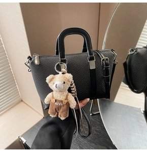 Detail of black woven texture crossbody bucket bag with a cute plush bear charm accessory