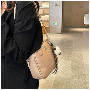 Detail of a chic beige shoulder bag with metal logo, zip pocket, and plush lamb pendant