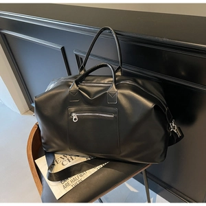 Détail du sac de voyage en cuir noir avec fermetures éclair argentées sur chaise