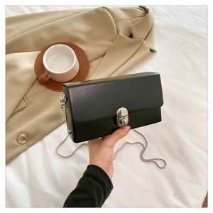 Close-up of black crossbody box bag with silver lock and chain strap held by hand