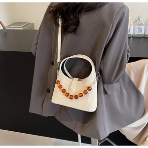 Detail of cream white bucket bag with amber beaded chain on a dark grey blazer