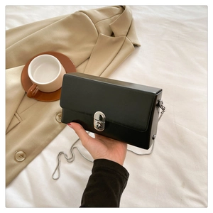 Detail of a black mini box bag with silver twist lock and chain strap against suit