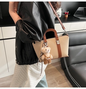 Detail of straw woven shoulder bag with brown leather handles and a bear charm pendant