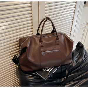 Vue détaillée du grand sac de voyage marron avec bandoulière en tissu sur siège en cuir
