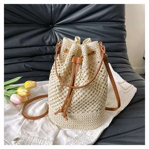 Detail view of woven straw bucket bag with brown leather drawstring and shoulder strap