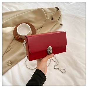 Close-up of red rectangular chain bag with silver oval twist lock on beige fabric