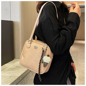 Close-up of apricot crossbody bag with silver logo, zipper and plush charm detail