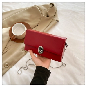 Close-up of a bright red box bag featuring a silver rotary lock and thin chain strap