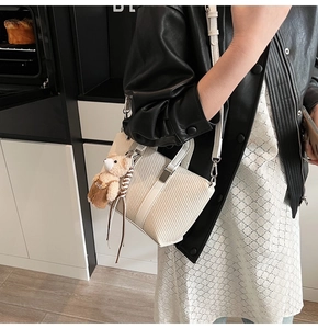 Close-up of white woven texture bag with leather trim and brown bear charm